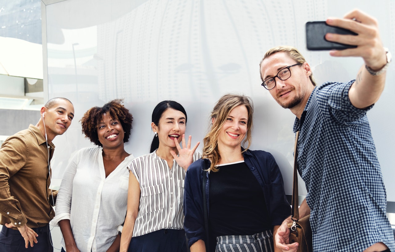 Group of five people taking a selfie in front of a white wall.